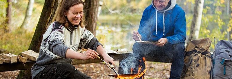 Eine Frau und ein Mann machen über dem Lagerfeuer im Wald ein Essen
